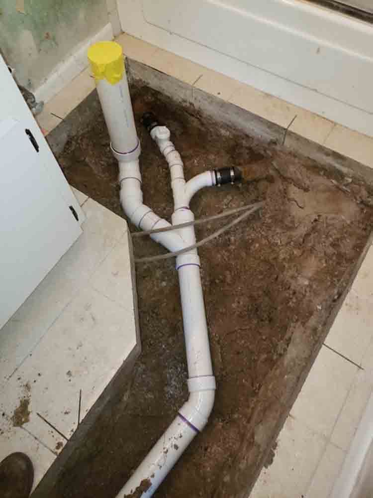 Exposed white PVC drain pipes in a dirt-floored utility area with a capped vertical vent pipe.
