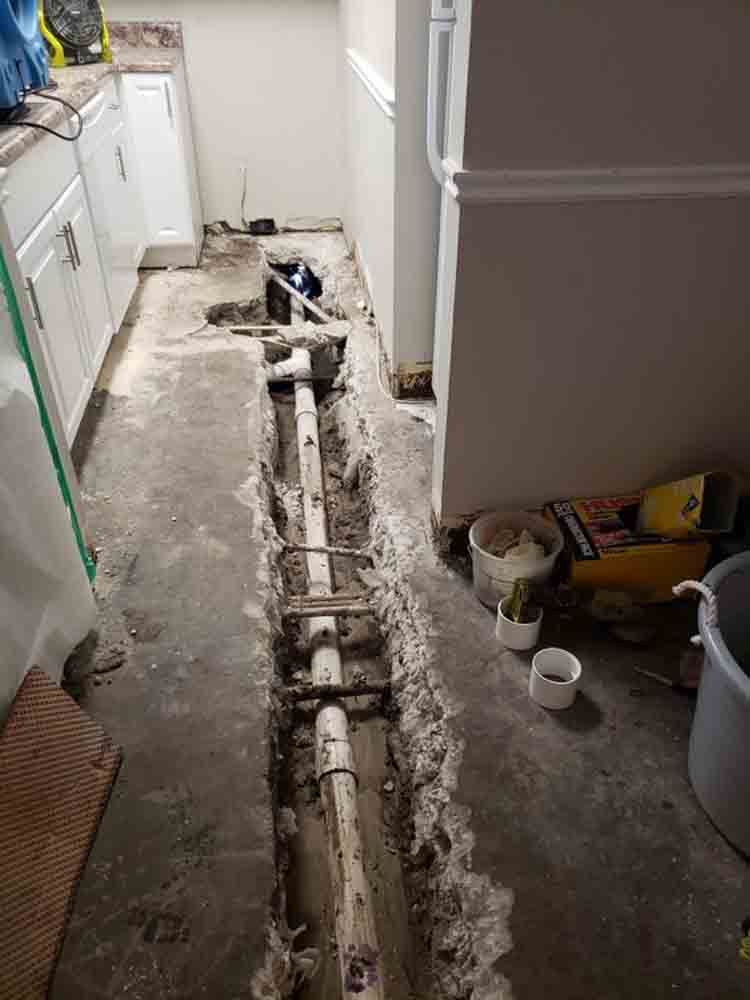 Kitchen floor cut open for plumbing repair, exposing pipes along the center aisle.