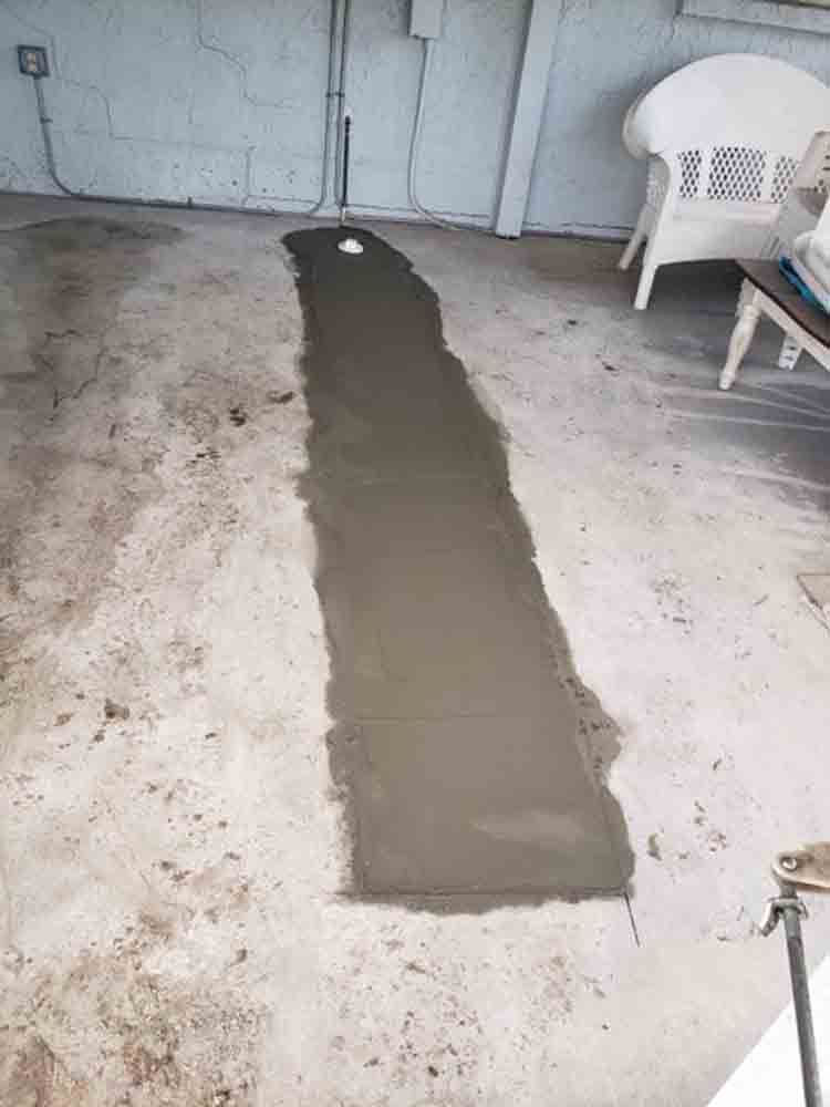 Fresh concrete patch on a worn garage floor beside a white plastic chair