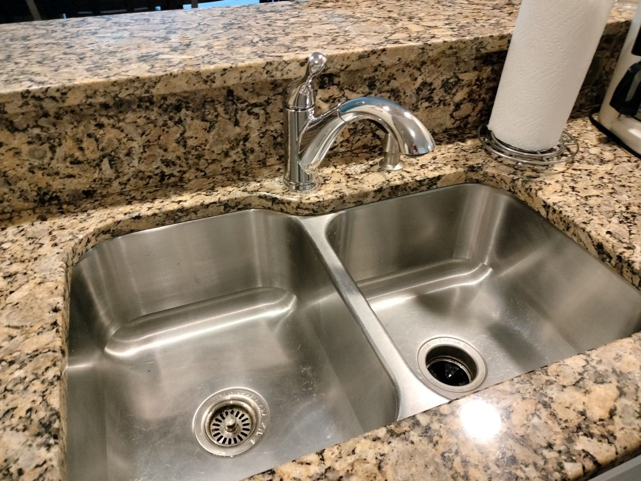 Stainless steel double kitchen sink with chrome faucet and speckled granite countertop.