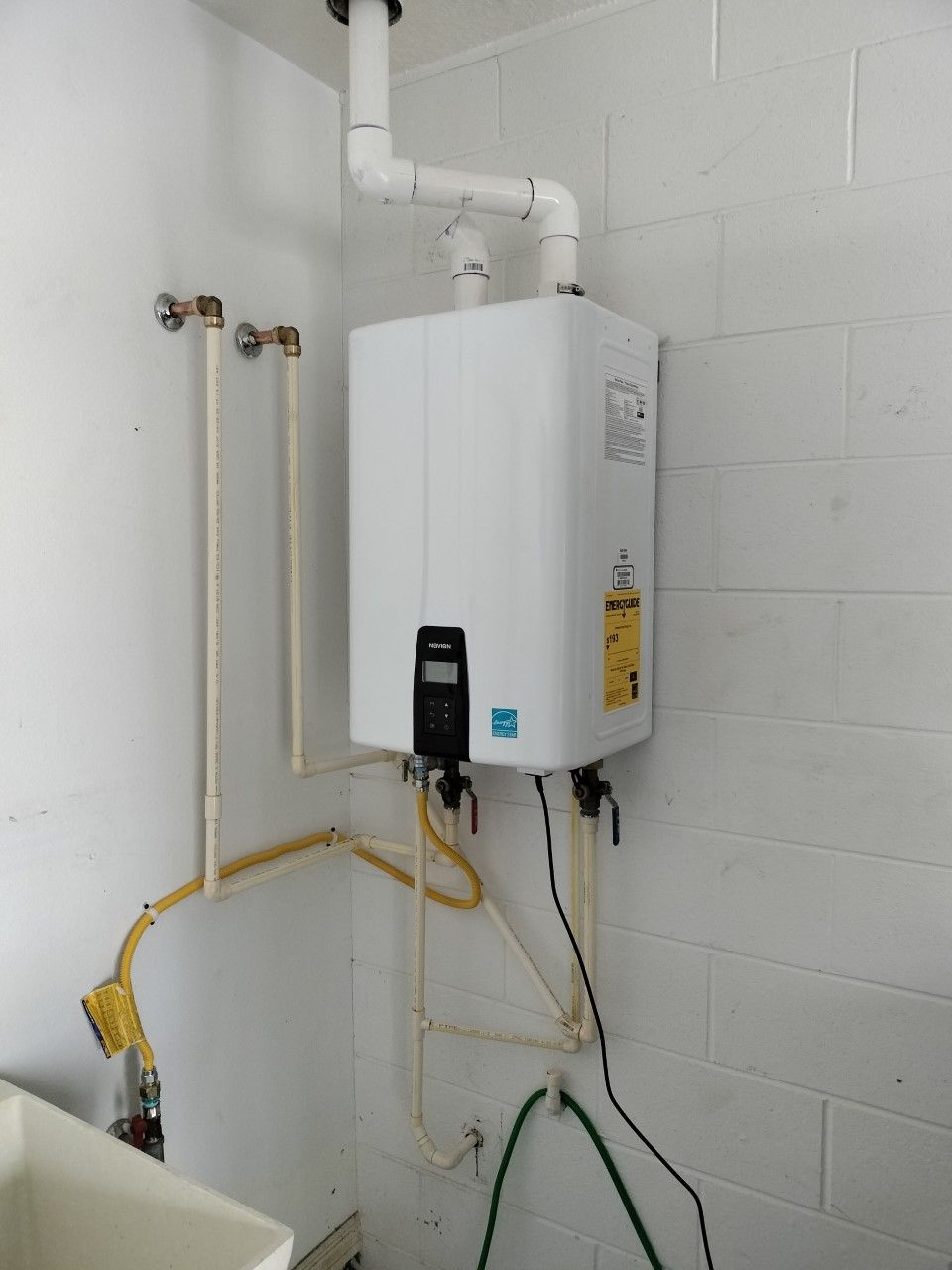 Wall-mounted white water heater with pipes and hoses in a utility room