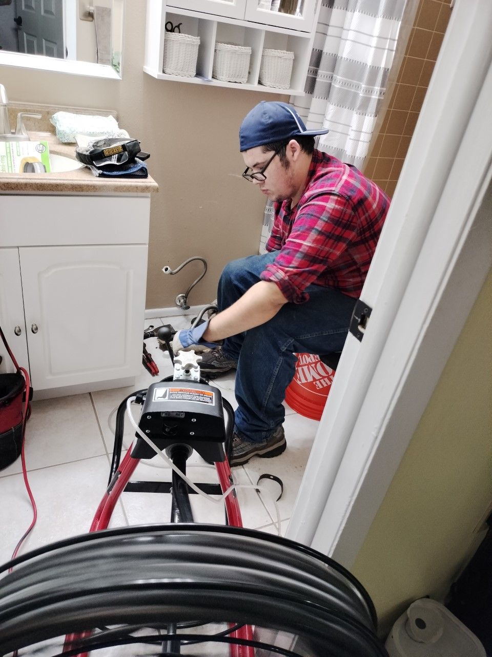 Worker in a plaid shirt and blue cap repairing plumbing in a small laundry room