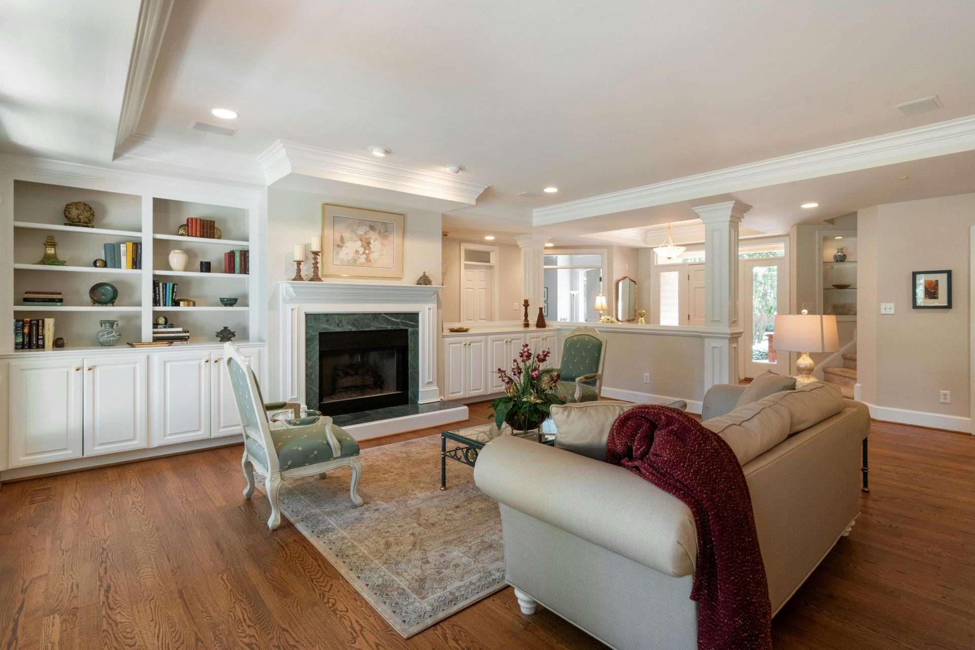 A living room with light hardwood floors, a beige sofa with a red throw, a fireplace, and built-in bookshelves.