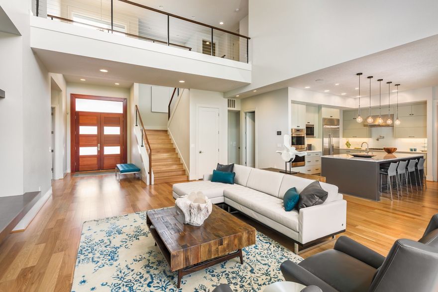 An open-concept living area with hardwood floors, a white sectional sofa, a wooden coffee table, and an adjacent kitchen.