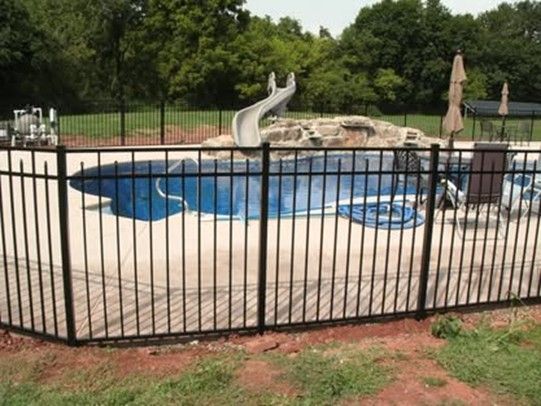 Black fenced-in swimming pool with a slide, surrounded by concrete and grass, trees in the background. Black fenced-in swimming pool with a slide, surrounded by concrete and grass, trees in the background.