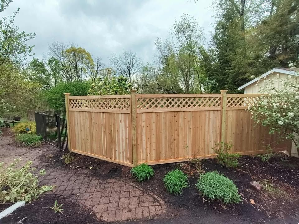 Wooden fence with lattice detail in a yard with landscaping and a small building.