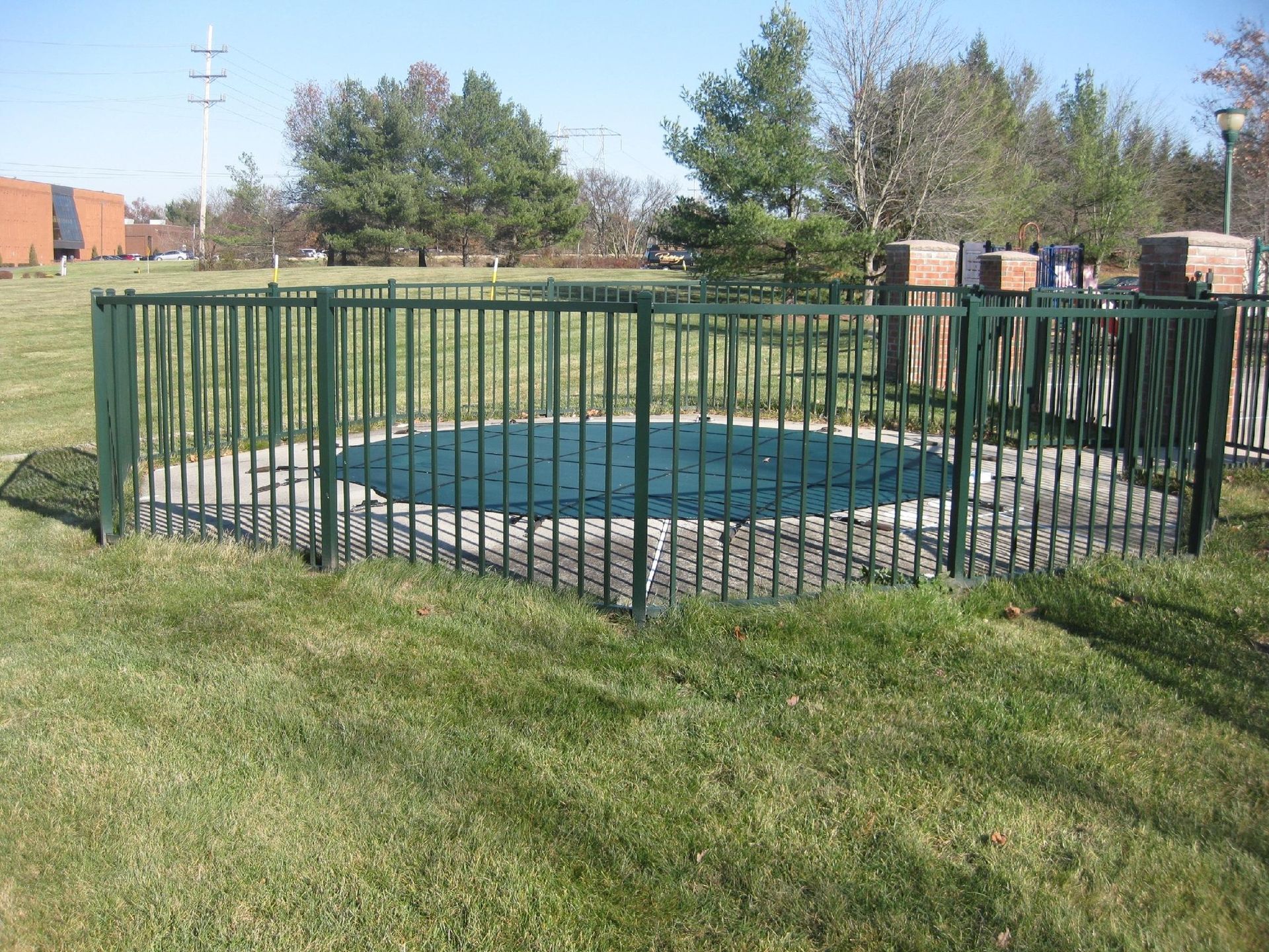 Green fenced-in trampoline on grass in a park setting.