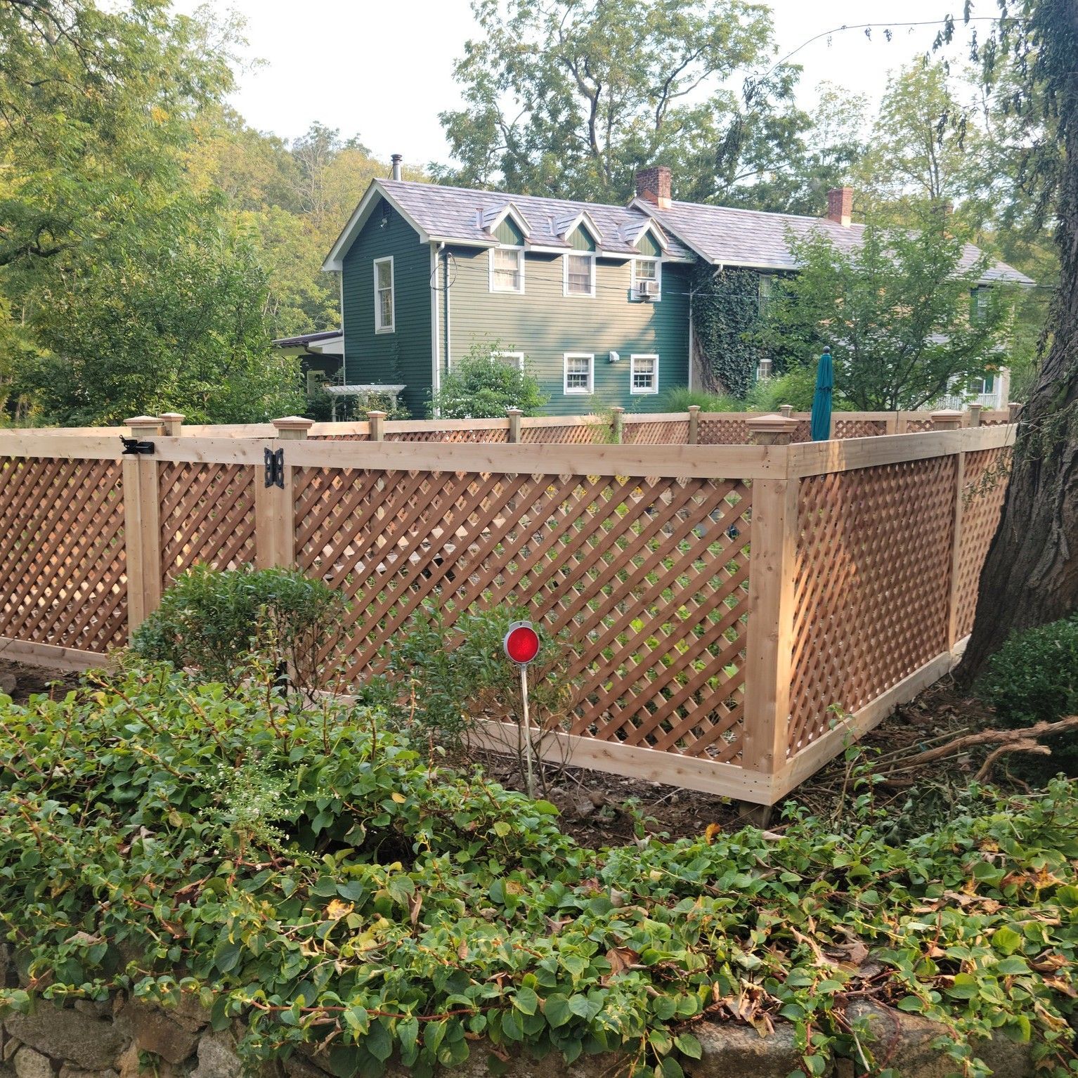 Wooden lattice fence surrounding a garden in front of a green house.