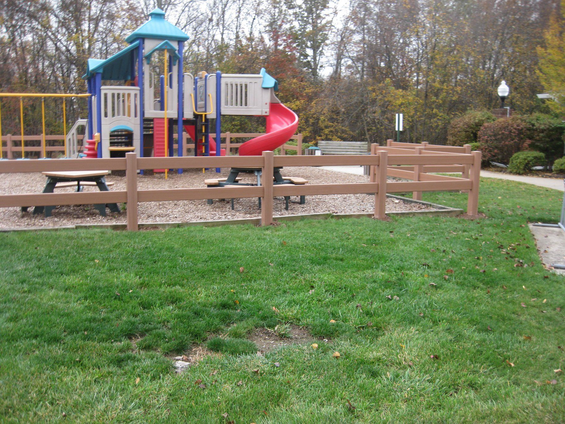 Playground with a red slide, brown fence, and green grass.
