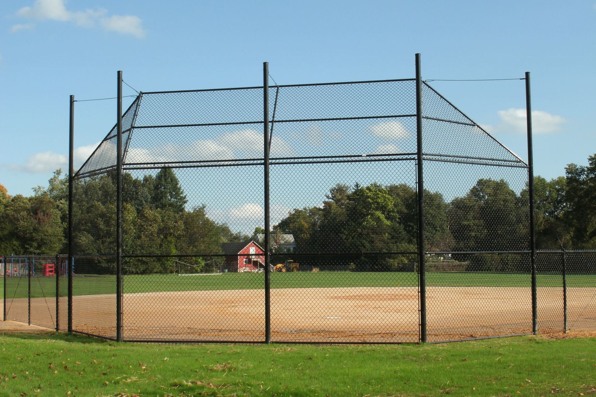 Baseball backstop with black netting and poles on a dirt field, green grass in foreground.