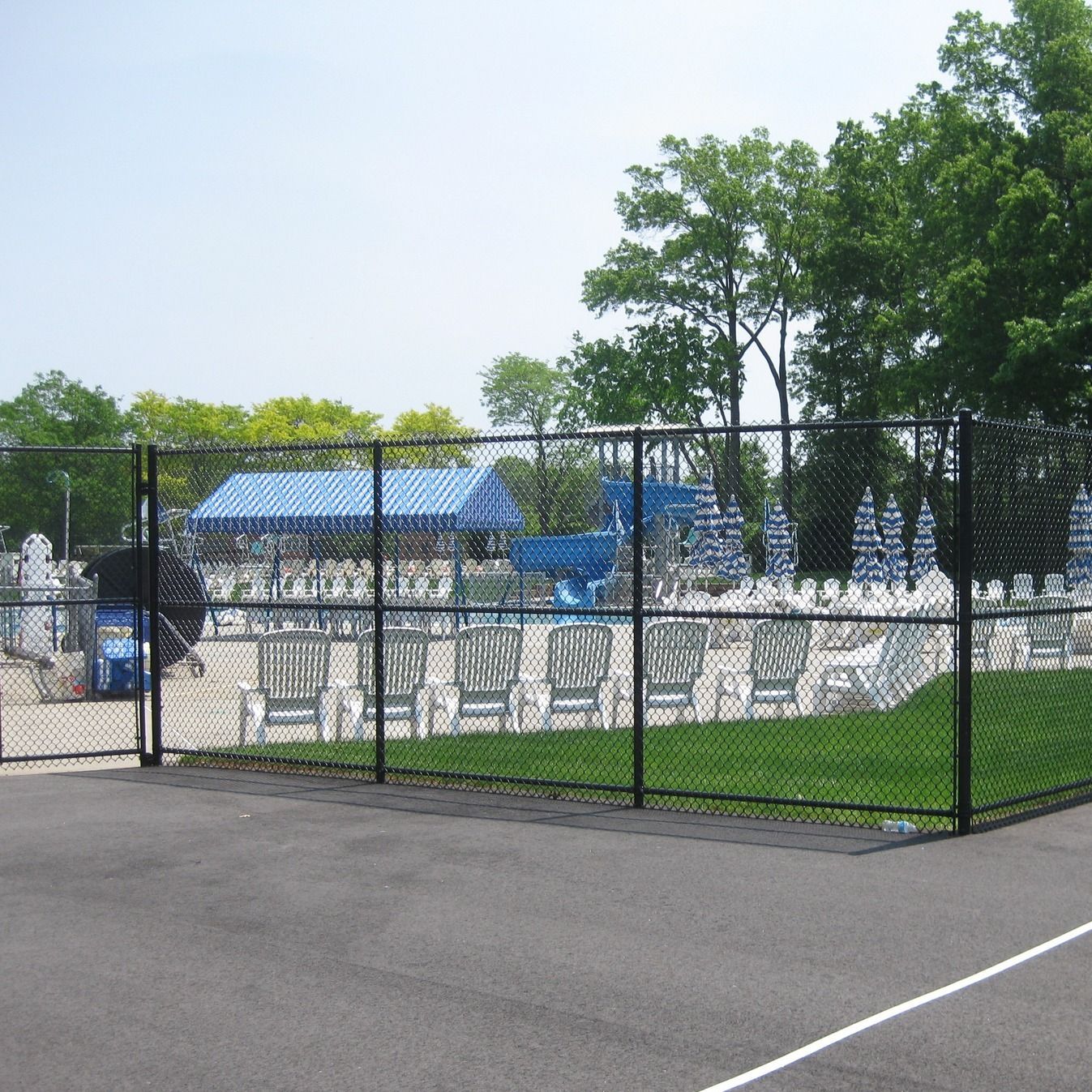 Black fence surrounding a pool area with lounge chairs and water slides on a sunny day.