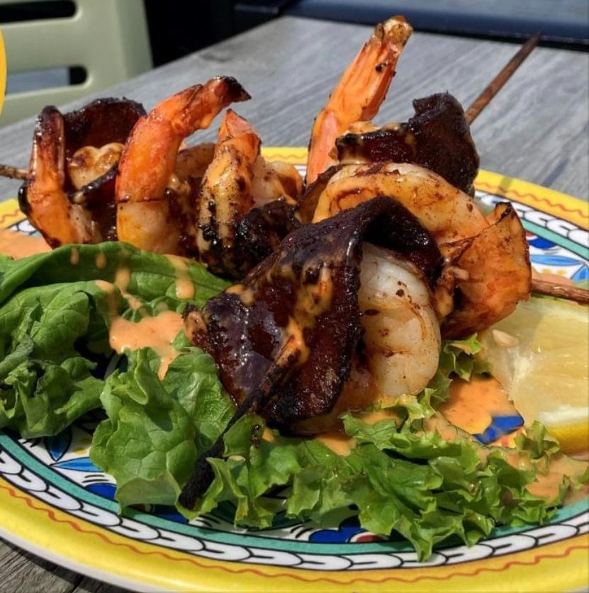 Grilled shrimp skewers over greens on a patterned plate, with sauce drizzled on top