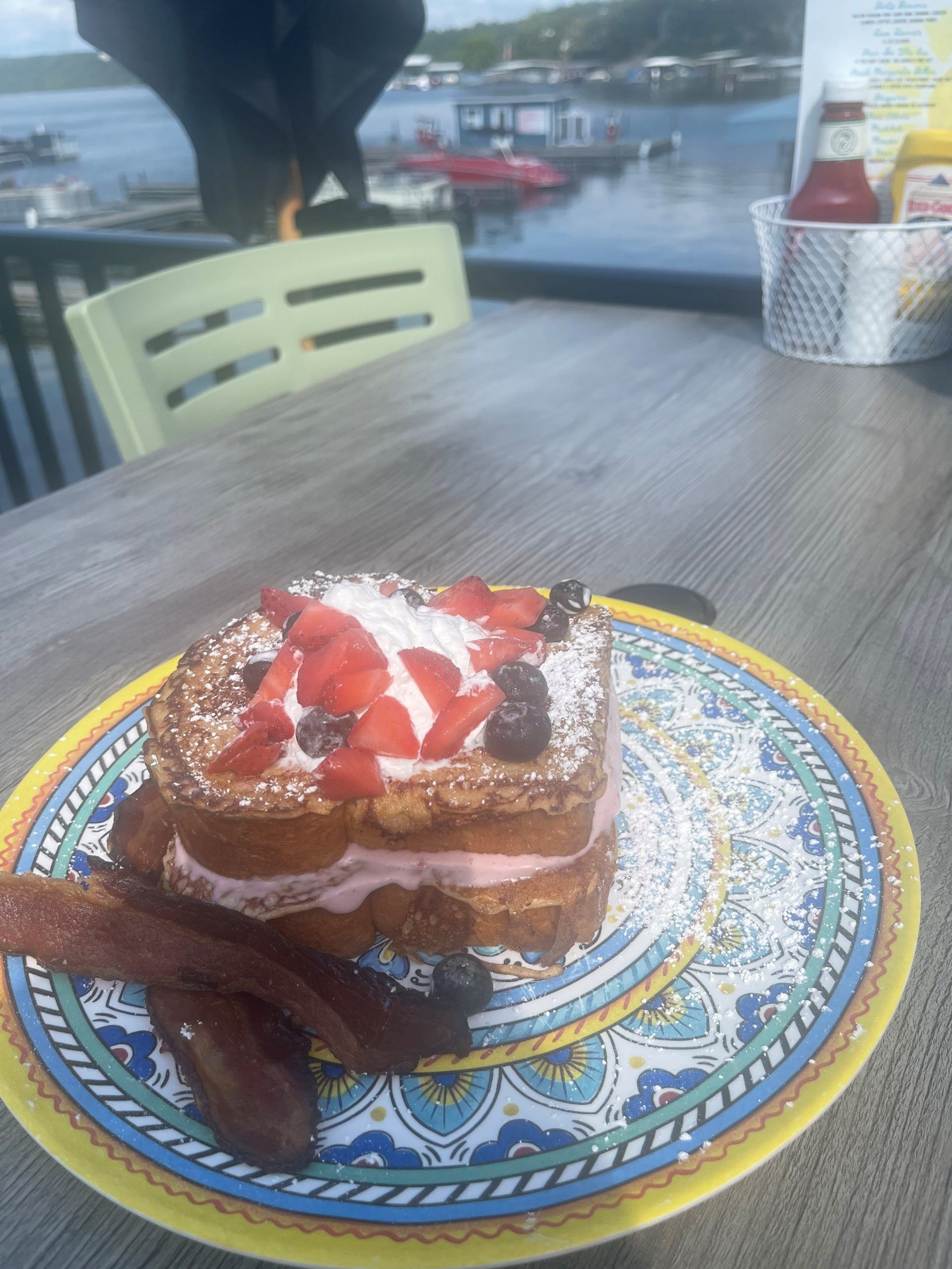 Chocolate dessert topped with strawberries and whipped cream on a decorative plate by the water.