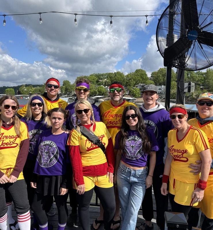 Group in purple and yellow jerseys posing outdoors at a sports field under a cloudy sky.