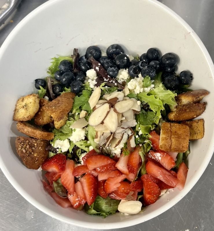 Bowl of salad with lettuce, strawberries, blueberries, almond slices, and croutons on a counter