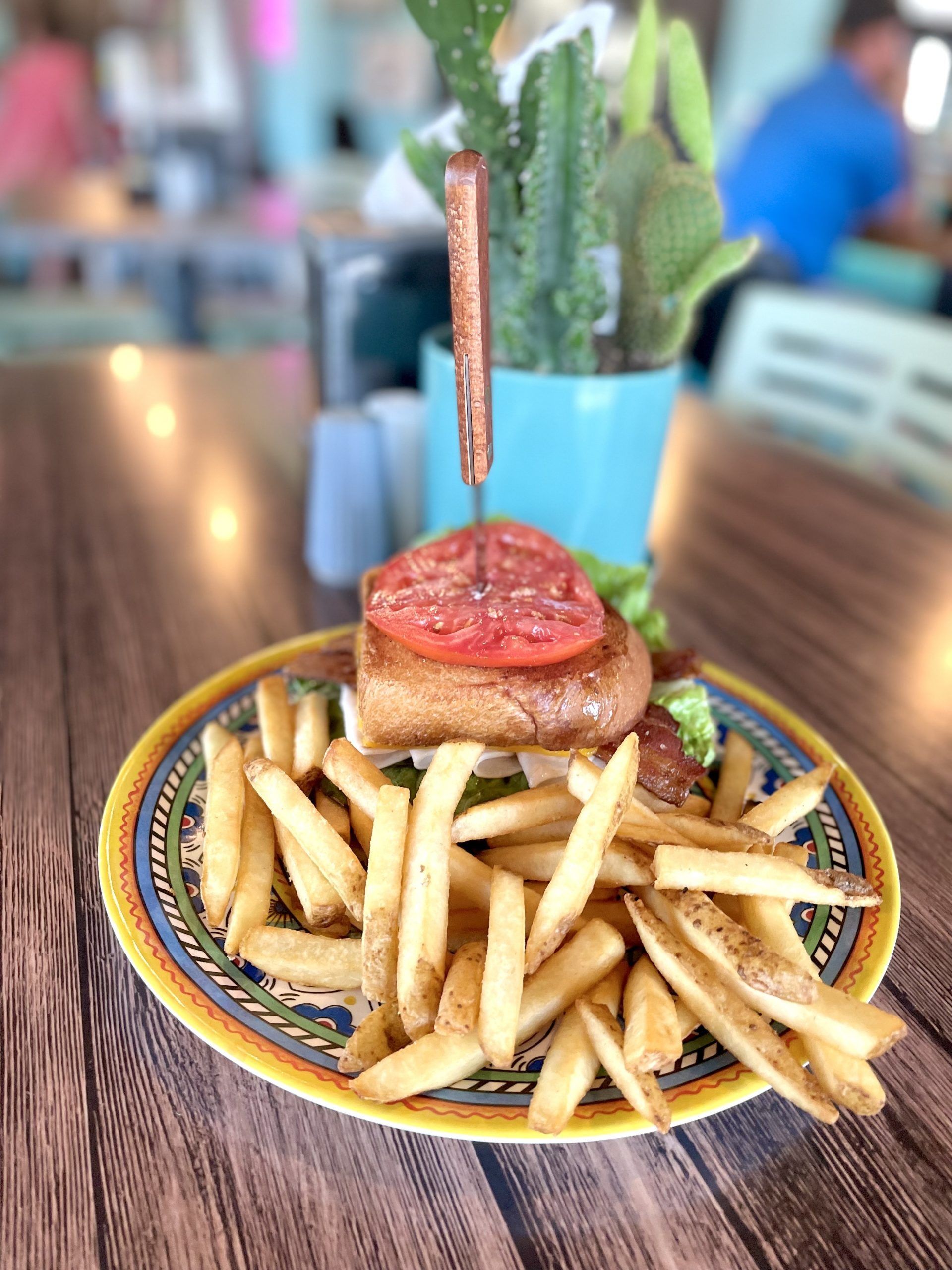 Plate of fries topped with a burger and tomato slice on a colorful restaurant table