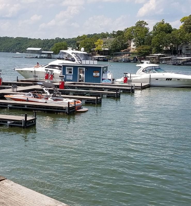 Boats docked at a lakeside marina on calm water under a partly cloudy sky