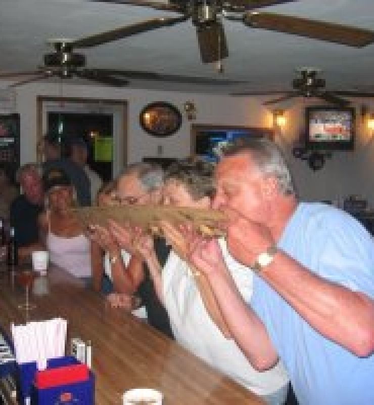 People at a bar toasting with large wooden horns, seated at a counter under ceiling fans.