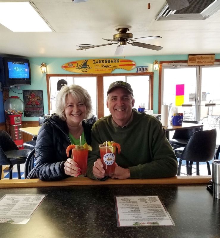 Two people smiling at a bar, holding colorful drinks in a casual restaurant.