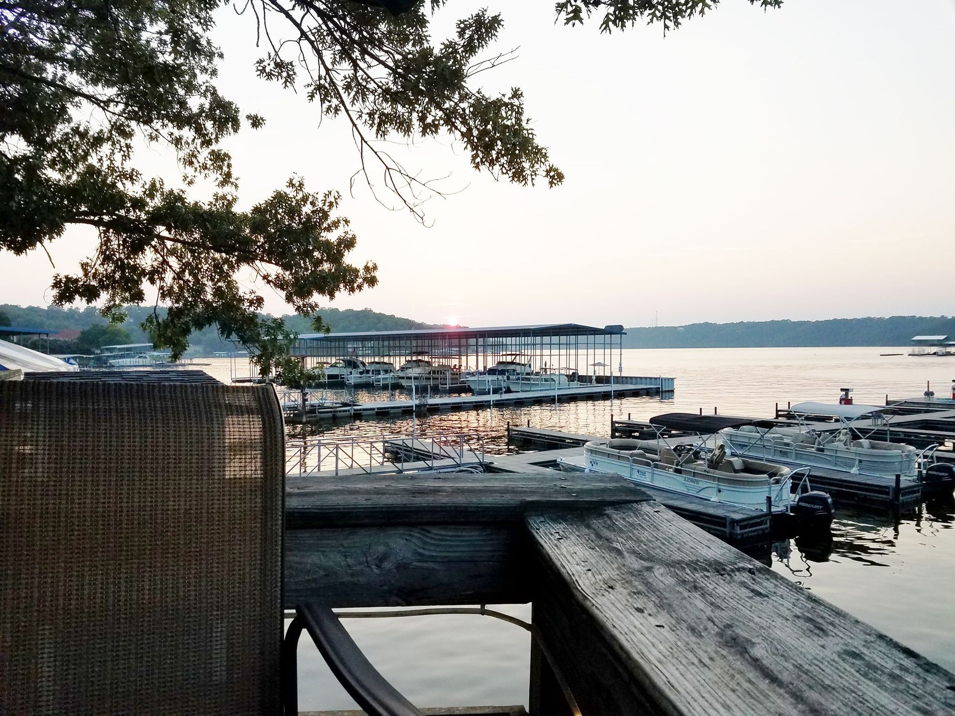 Lakefront marina with wooden docks at sunset, framed by tree branches and calm water