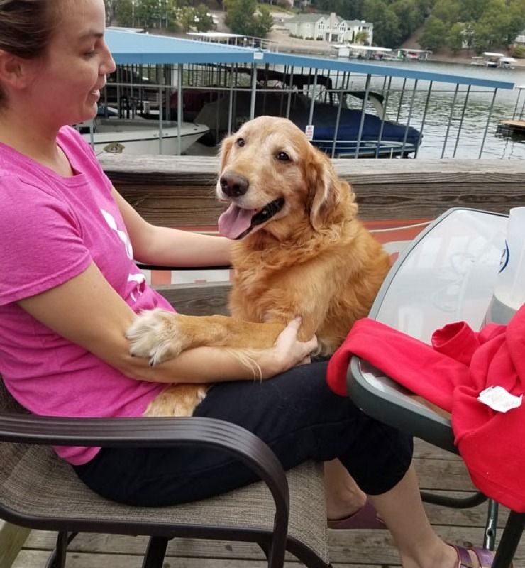 Woman in pink shirt holding a happy golden retriever on a dock by the water