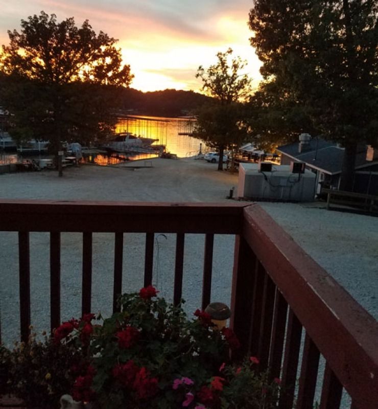 Sunset over a calm lake, seen from a deck with wooden railing and flowers in the foreground