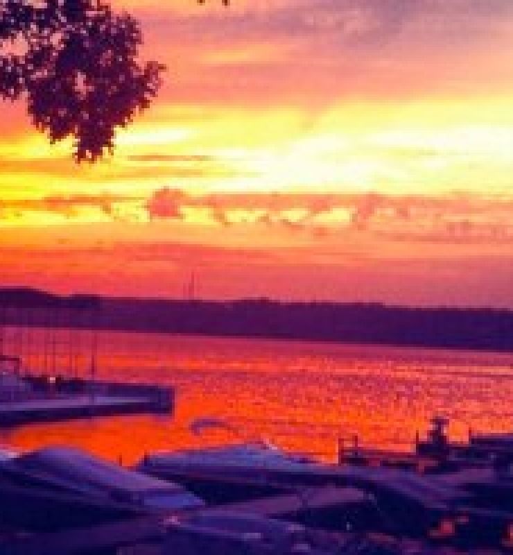 Sunset over a calm lake with orange-pink sky and silhouetted boats at the shore