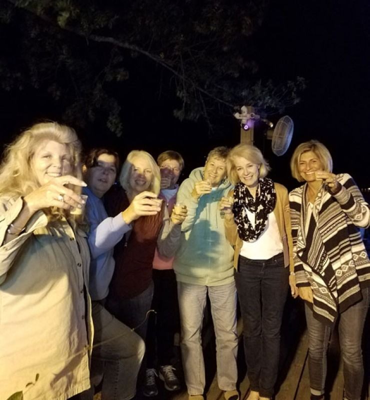 Group of people holding drinks outdoors at night, smiling and posing in dim light