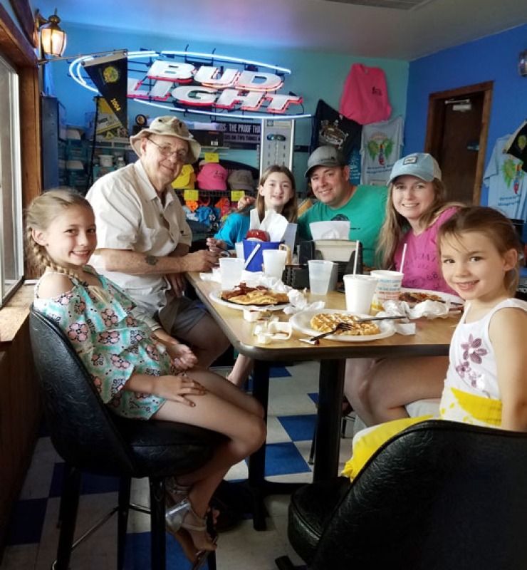 Family gathered around a restaurant table, smiling and eating in a colorful booth area.