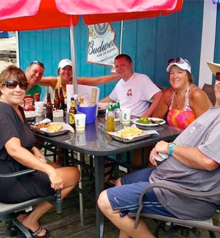 Group of people seated around an outdoor table at a colorful patio bar, drinking and chatting