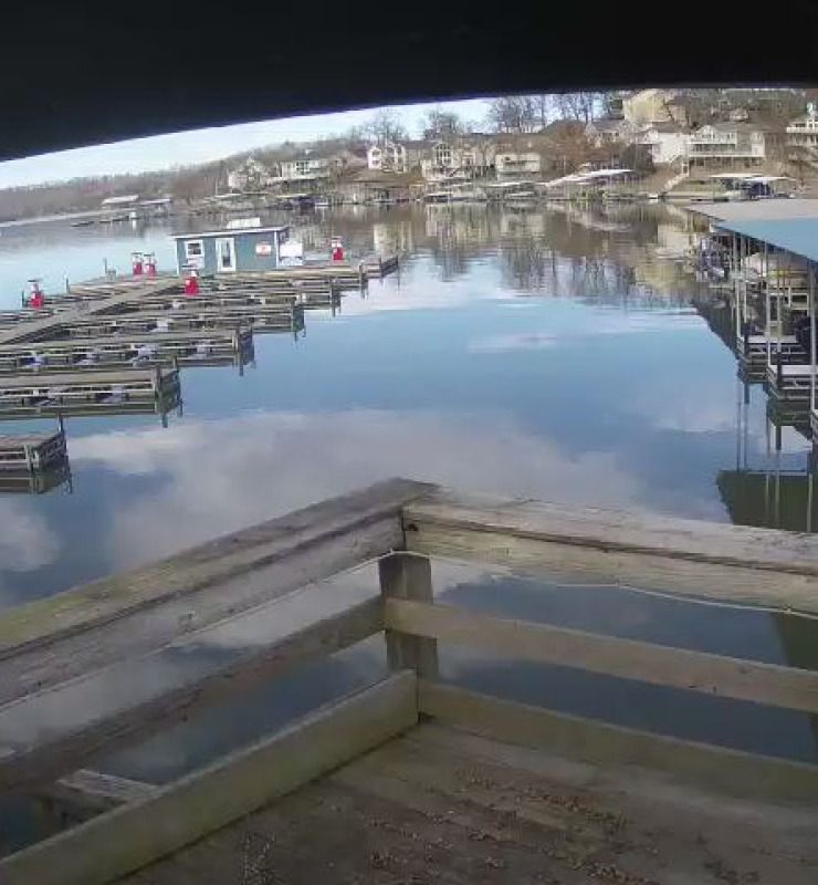 Calm marina with docked boats, wooden railings, and a reflective water view under a cloudy sky