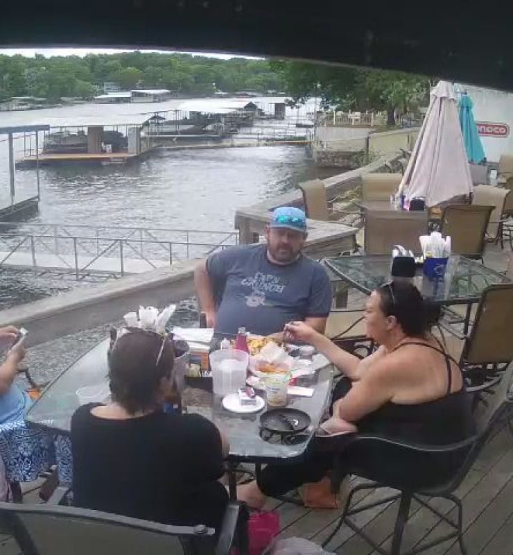People dining on a riverside deck with boats docked in the background
