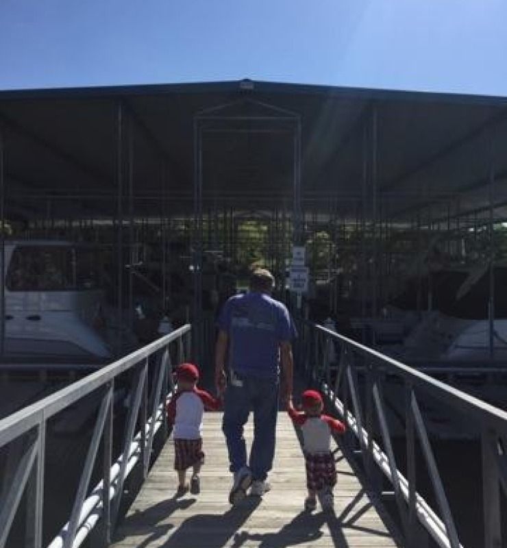 Man walking with two small children down a ramp toward a ferry terminal under a roof