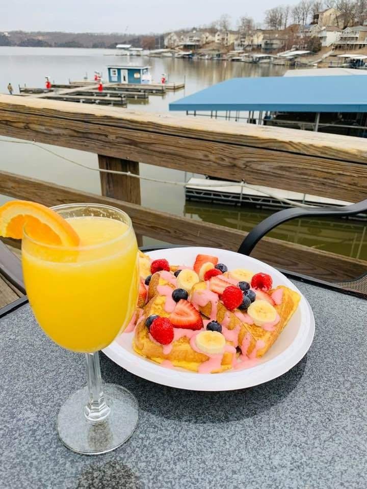 Orange cocktail and fruit tart on a table overlooking a waterfront pier on a cloudy day