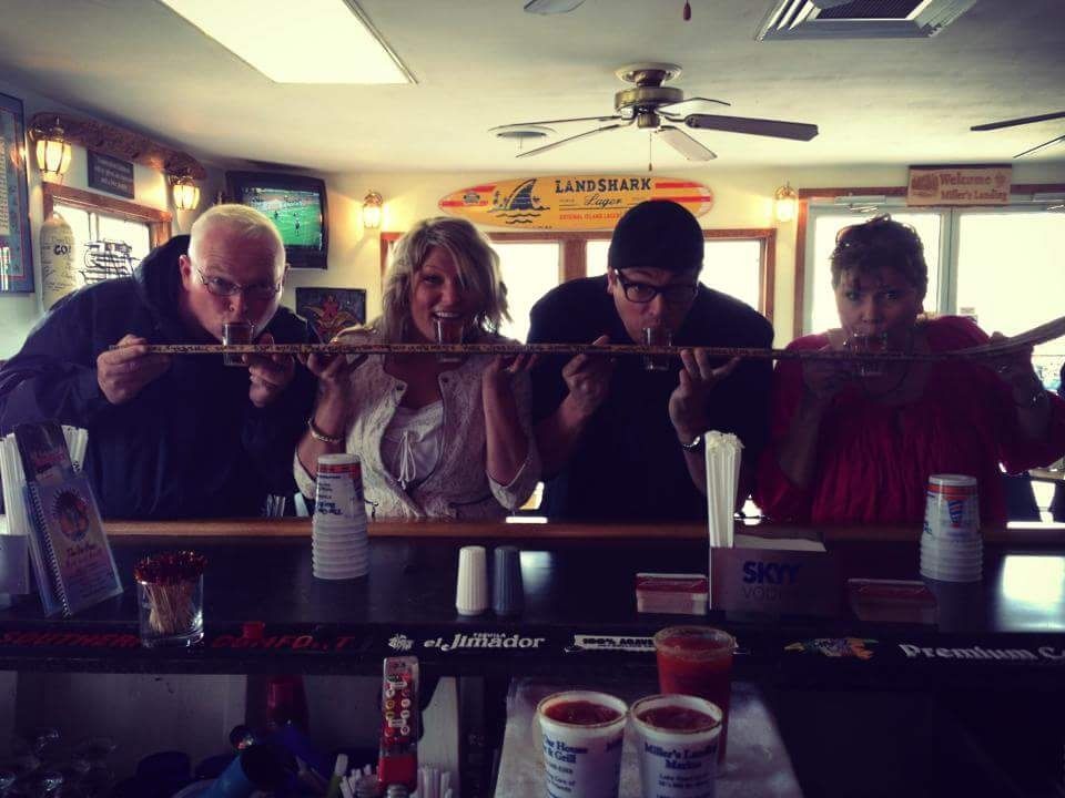 Four people lean over a bar counter, concentrating on shots or drinks in a dim indoor venue.