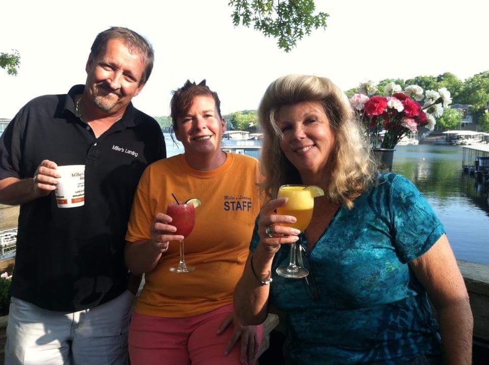 Three people holding drinks pose by a pool on a sunny day.