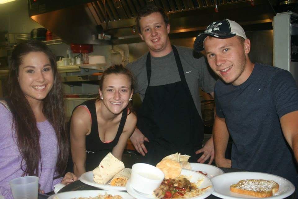 Four people smile at a restaurant table with plates of food in front of them.