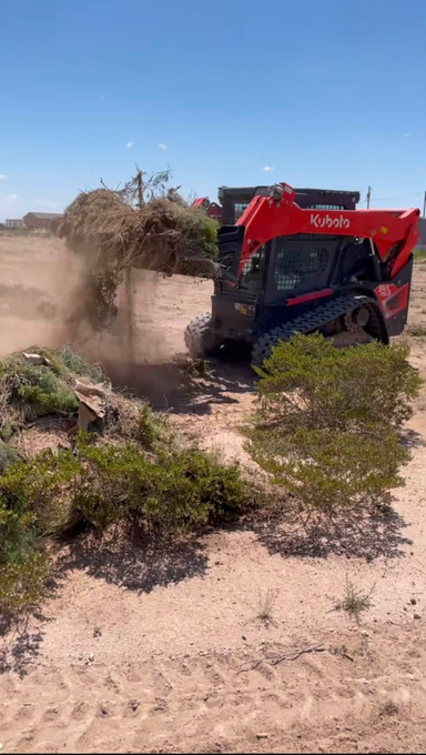 Red construction machine clearing brush and kicking up dust in a dry desert landscape.