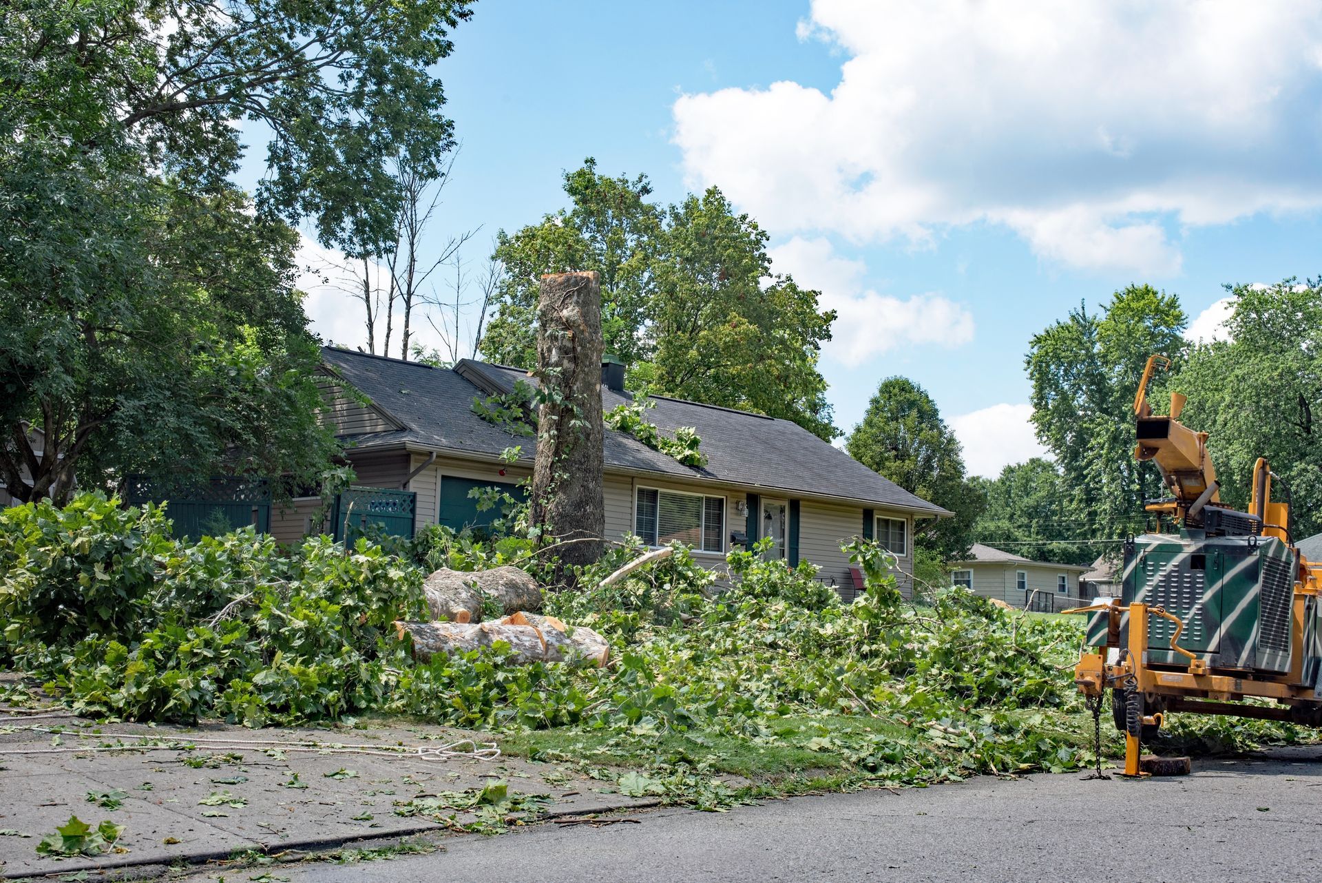 Storm damage cleanup with fallen tree branches blocking a street beside a house and utility truck