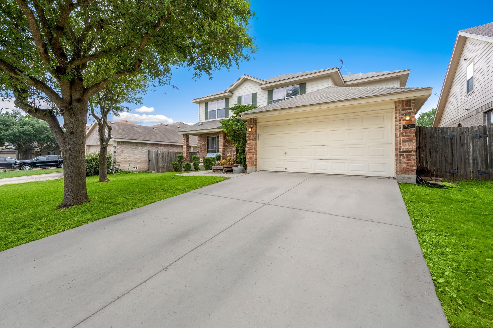 Suburban house with a two-car garage, long concrete driveway, and green lawn under a blue sky