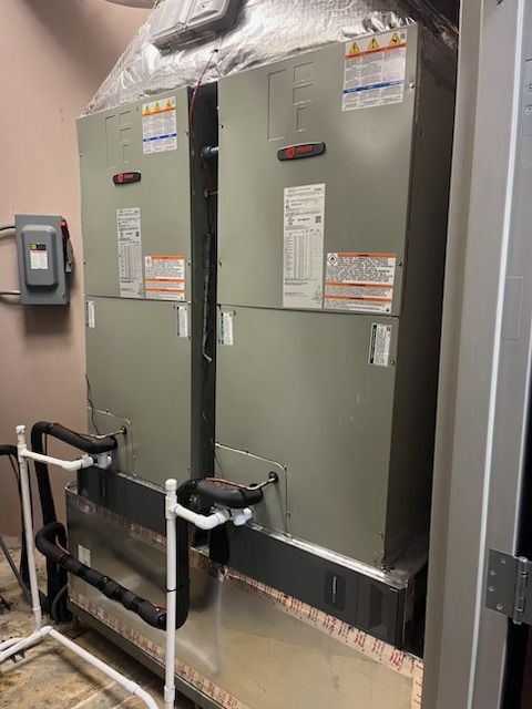 Two Trane HVAC air handler units standing side-by-side in a utility closet with white PVC condensate drain piping.