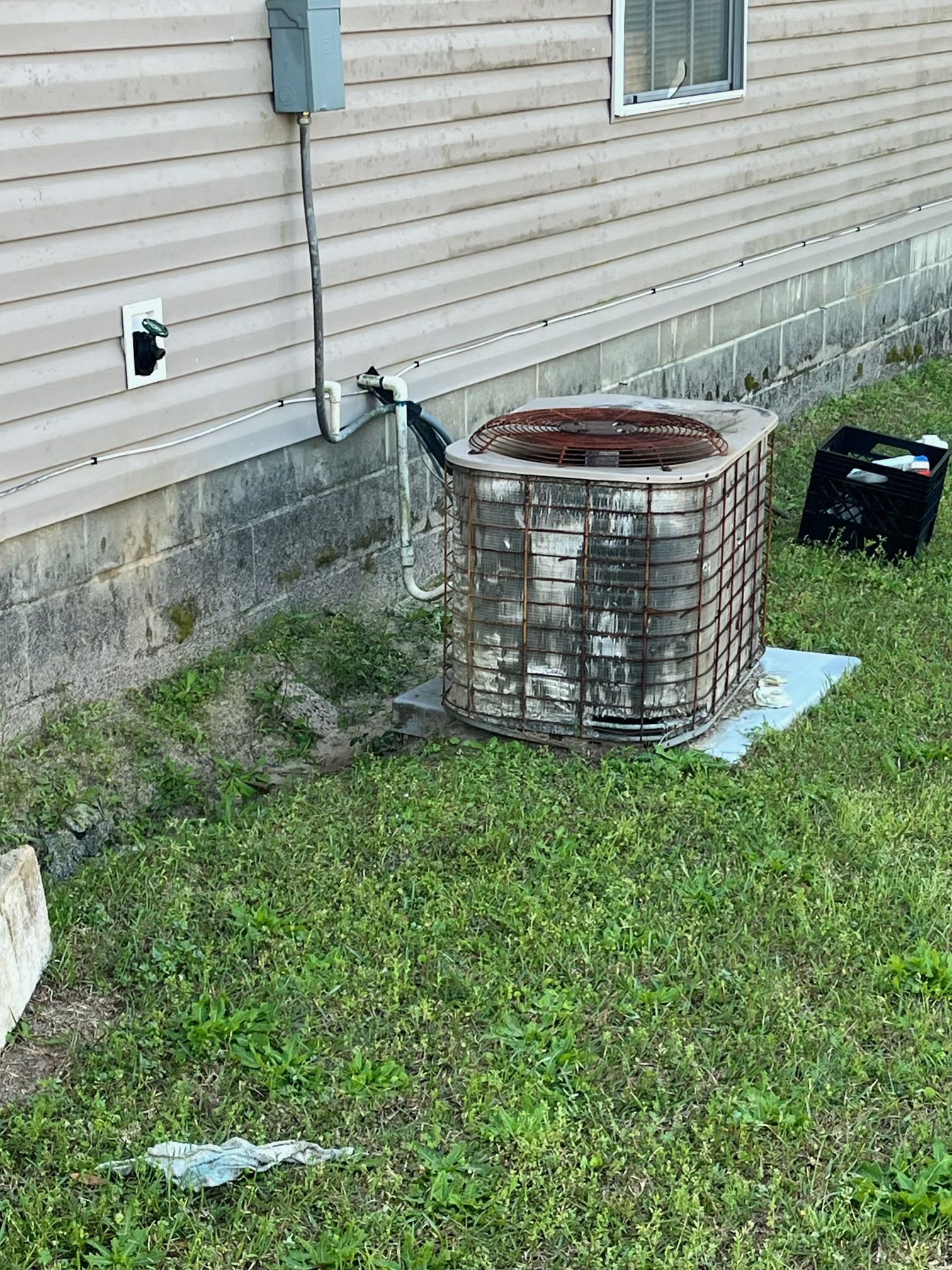 An outdoor air conditioning unit sits on a concrete pad against the tan siding of a home, missing its top fan cover.