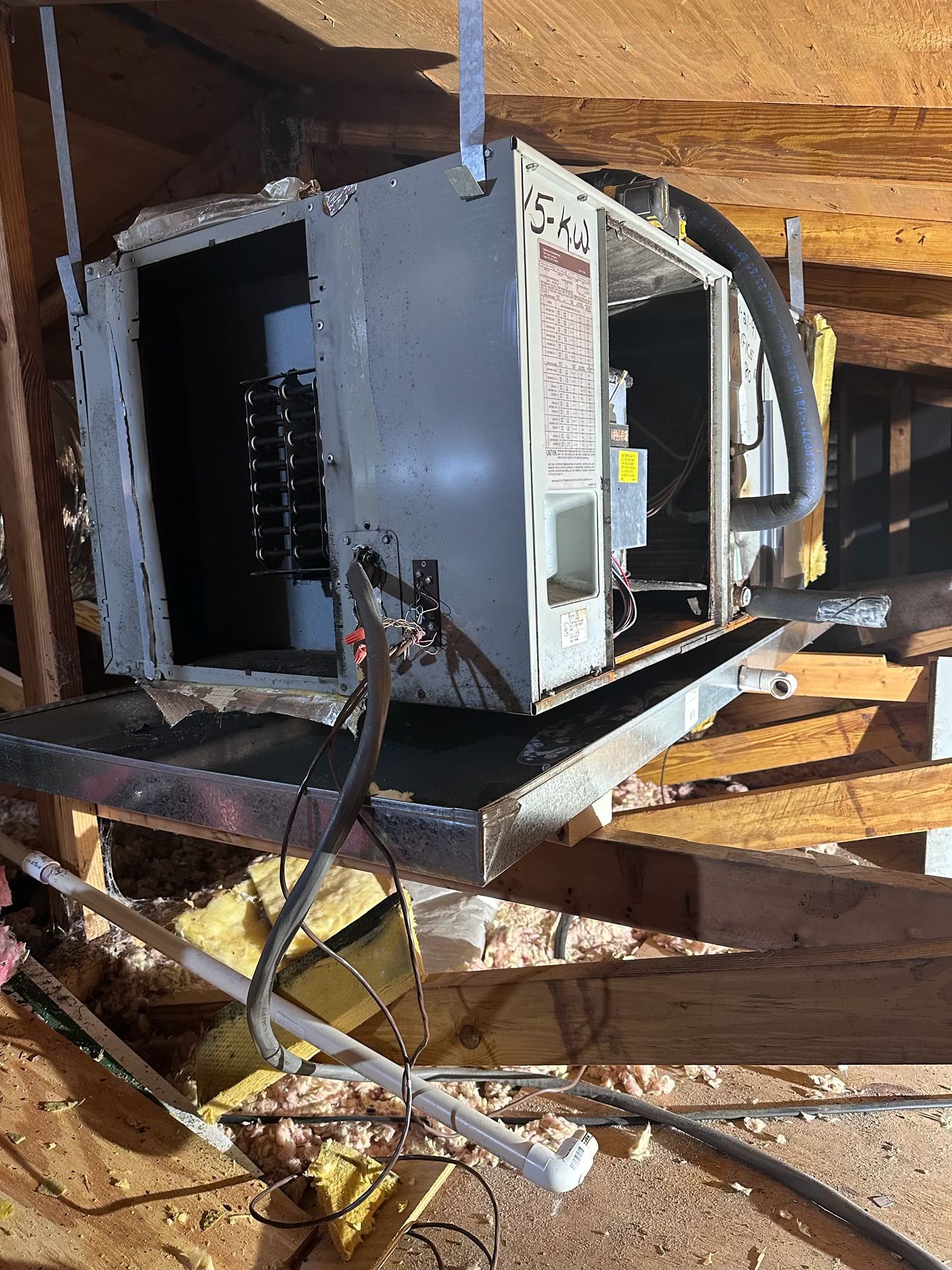An HVAC air handler suspended in an attic, showing internal components, electrical wiring, and a metal drain pan below.