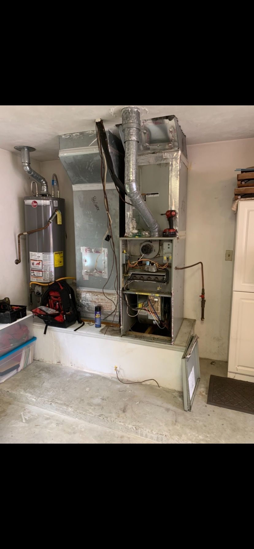 A utility room showing a gas water heater next to an opened HVAC furnace unit on a concrete platform.