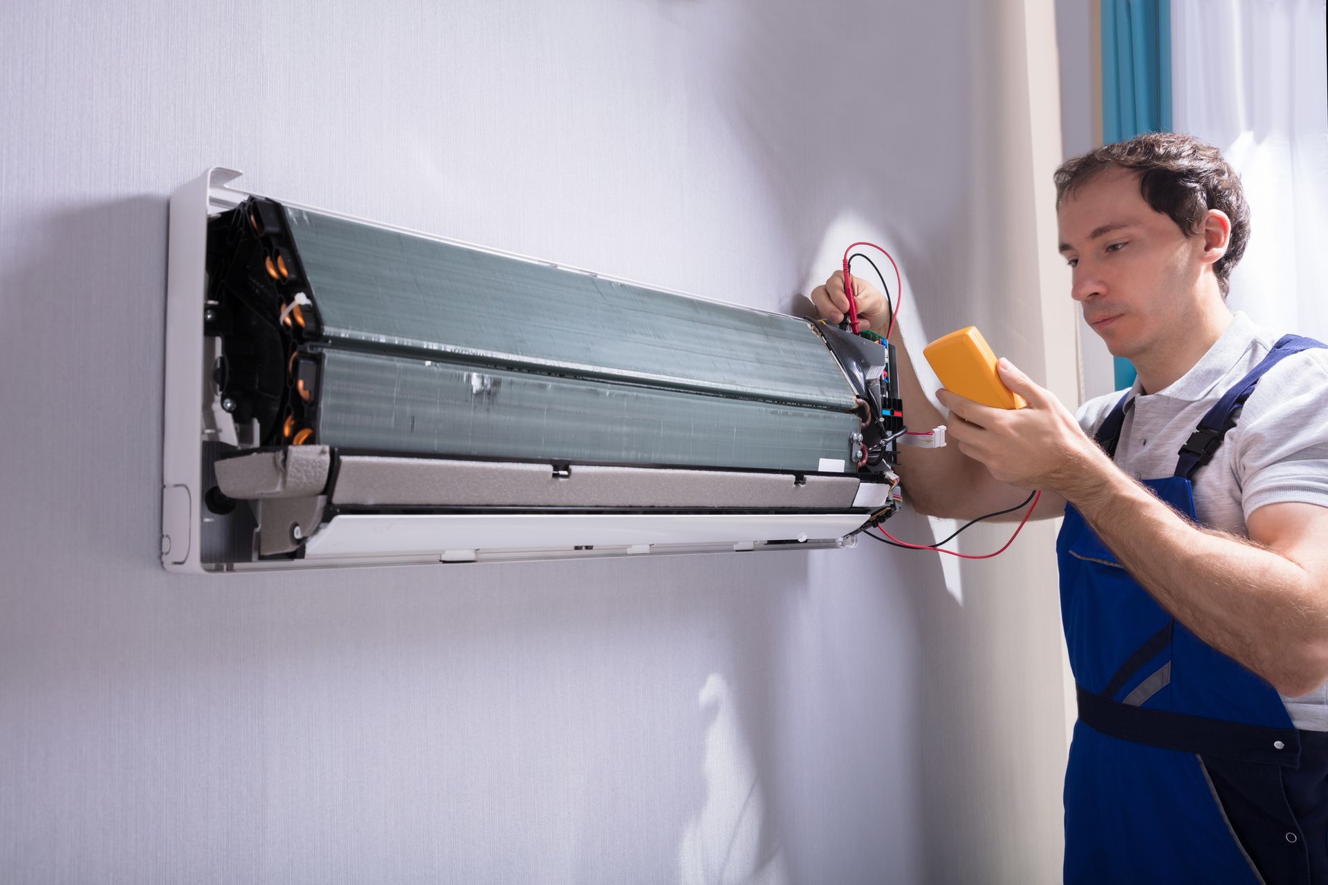 A man is fixing an air conditioner with a multimeter.