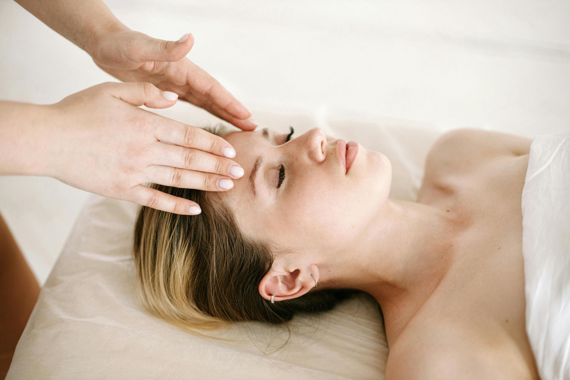 Mujer recibiendo un masaje facial, tumbada en una camilla. Se aplica suavemente las manos en la frente.