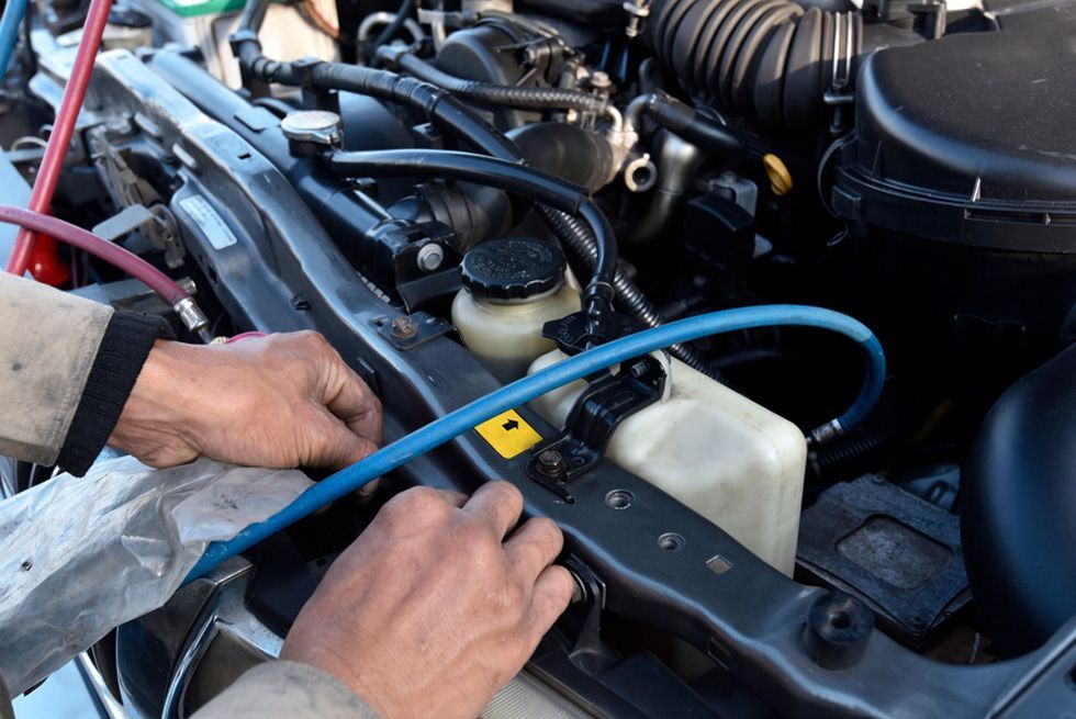 Hands Connecting Blue Hose to Car Engine for AC Service.