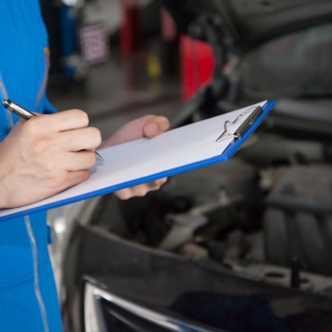 A Person Is Writing On A Clipboard In Front Of A Car — APPS Mechanical Port Macquarie In Port Macquarie, NSW
