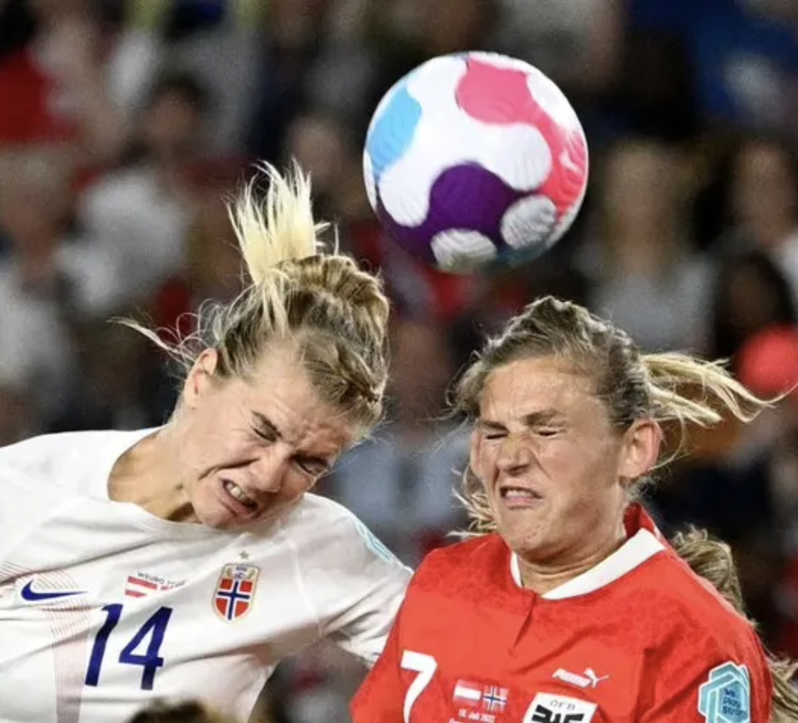 Two soccer players head a ball midair, one in white and one in red, during a match