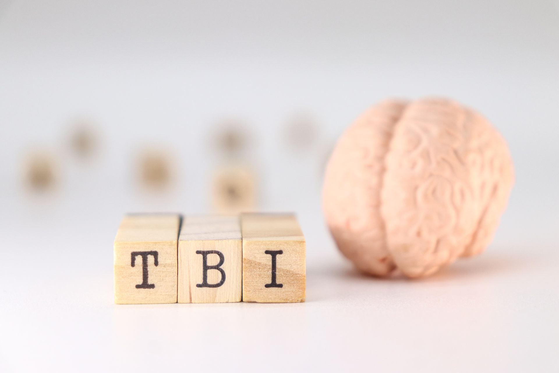 Wooden blocks spelling TBI beside a pink brain model on a white background